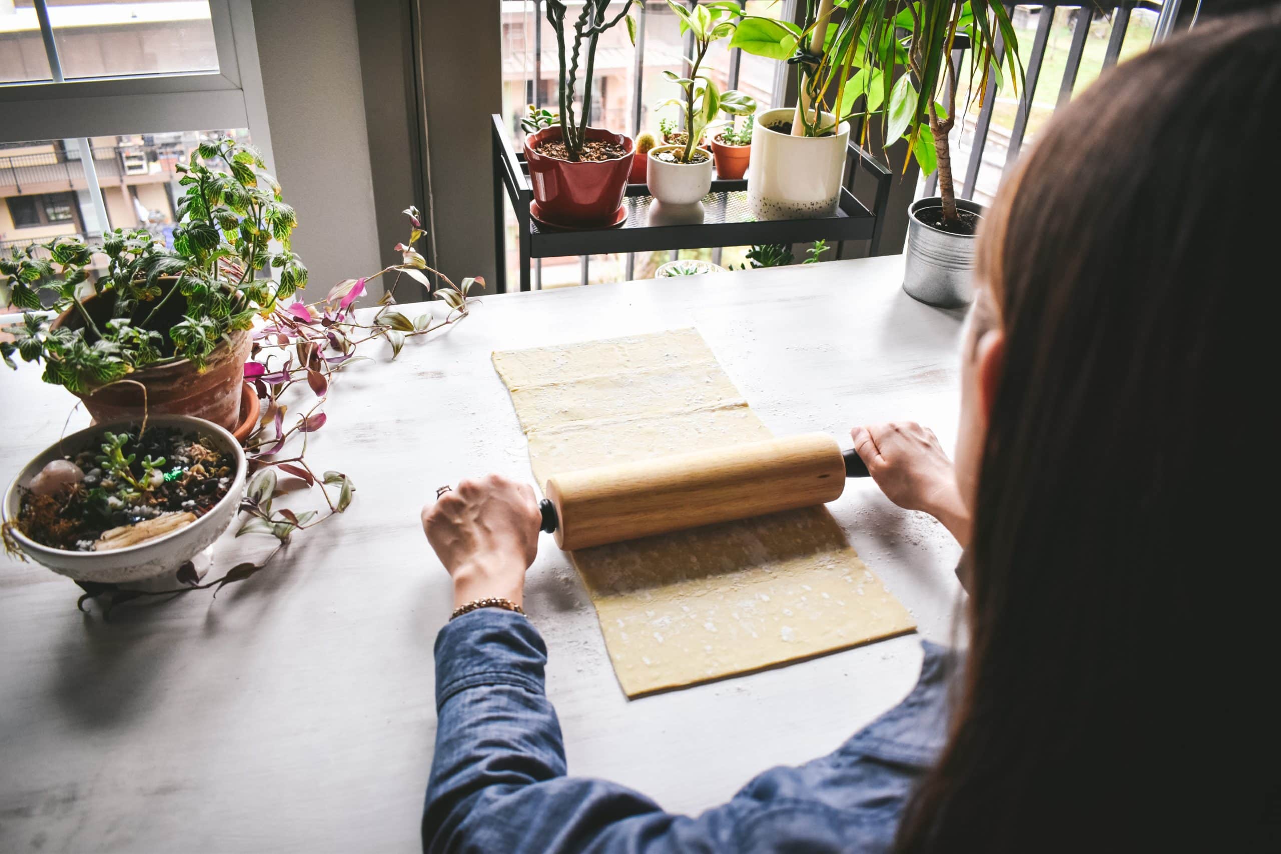 A girl rolling out a sheet of puff pastry dough on a white table.
