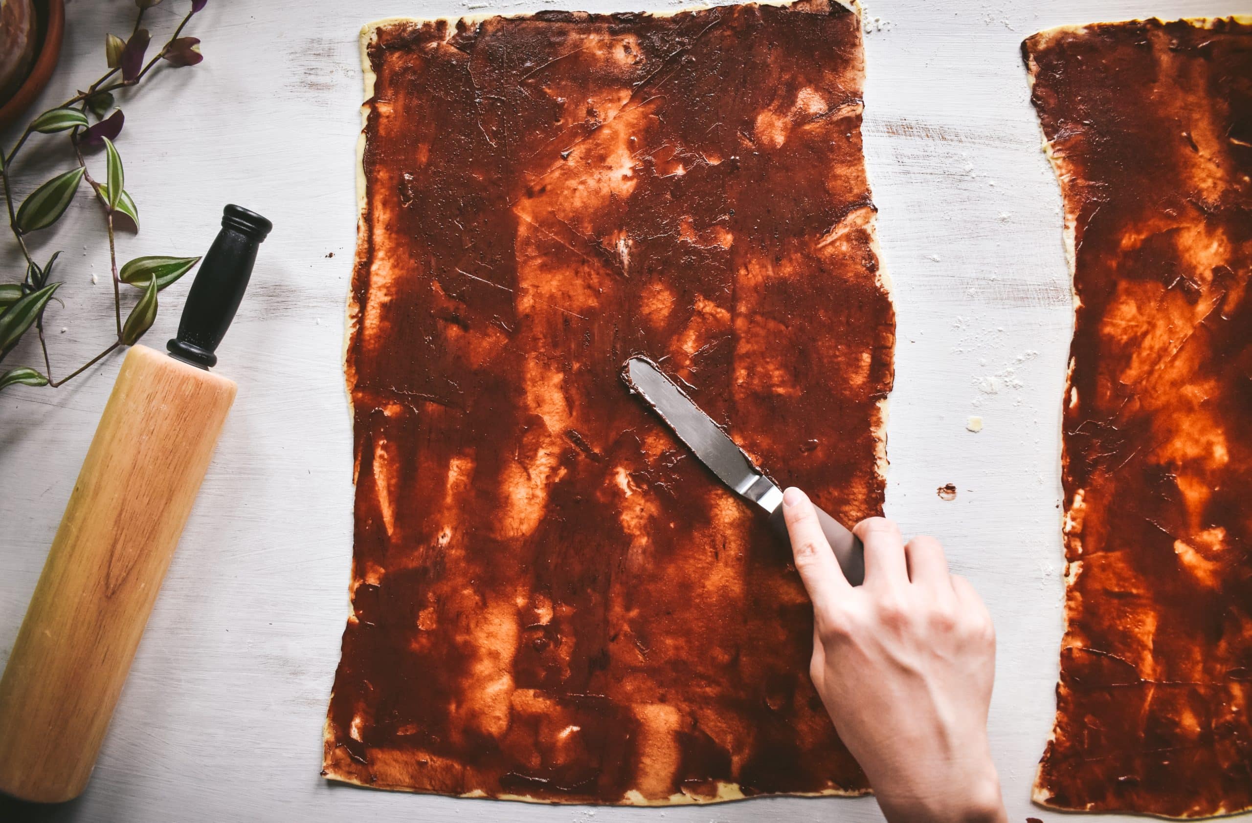 A hand smoothing softened butter and cocoa powder on two sheets of puff pastry dough.