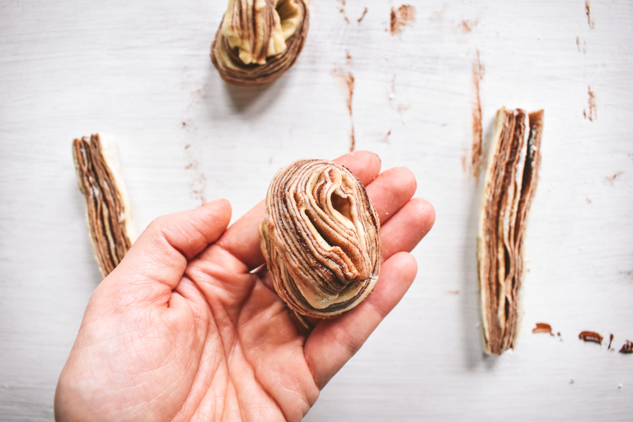 A hand holding an unbaked cruffin made with swirled puff pastry and cocoa powder.