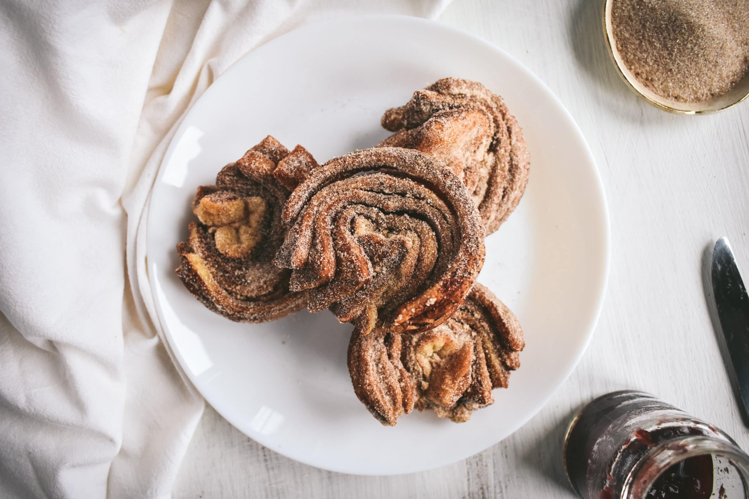 Four cruffins piled onto a white plate next to a white linen.
