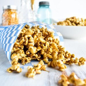 Golden caramel corn spilling out of a paper cone on a light table.