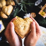 A hand holding a pumpkin pastie in the shape of a heart.