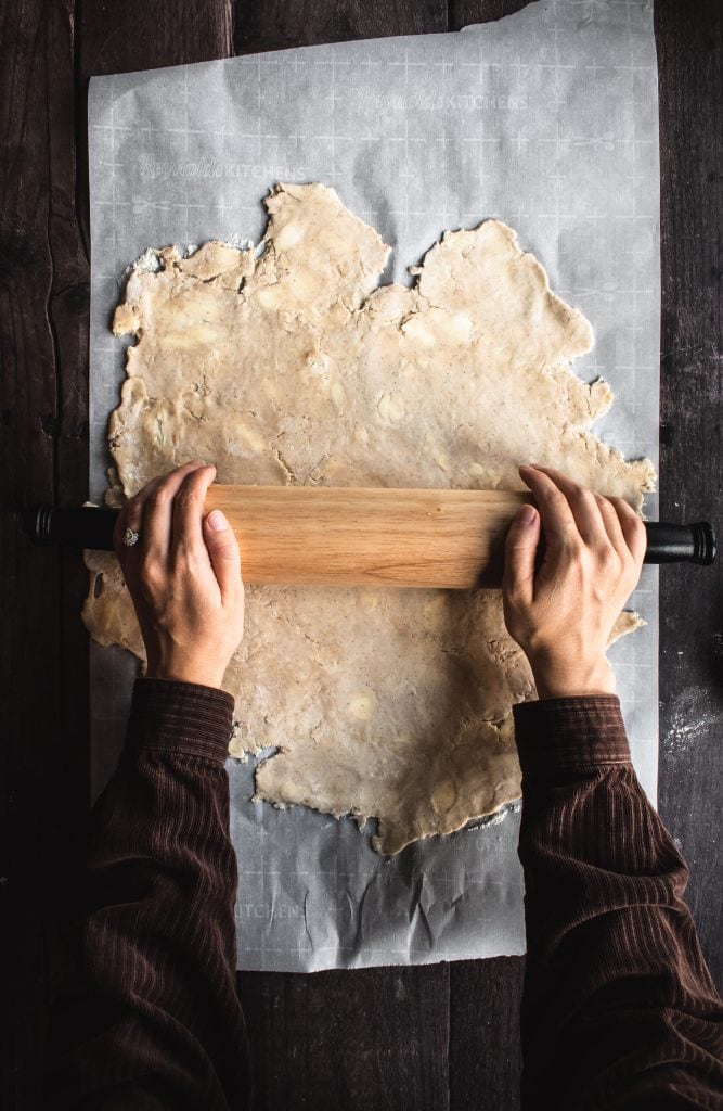 Two hands rolling out pie dough with a rolling pin.