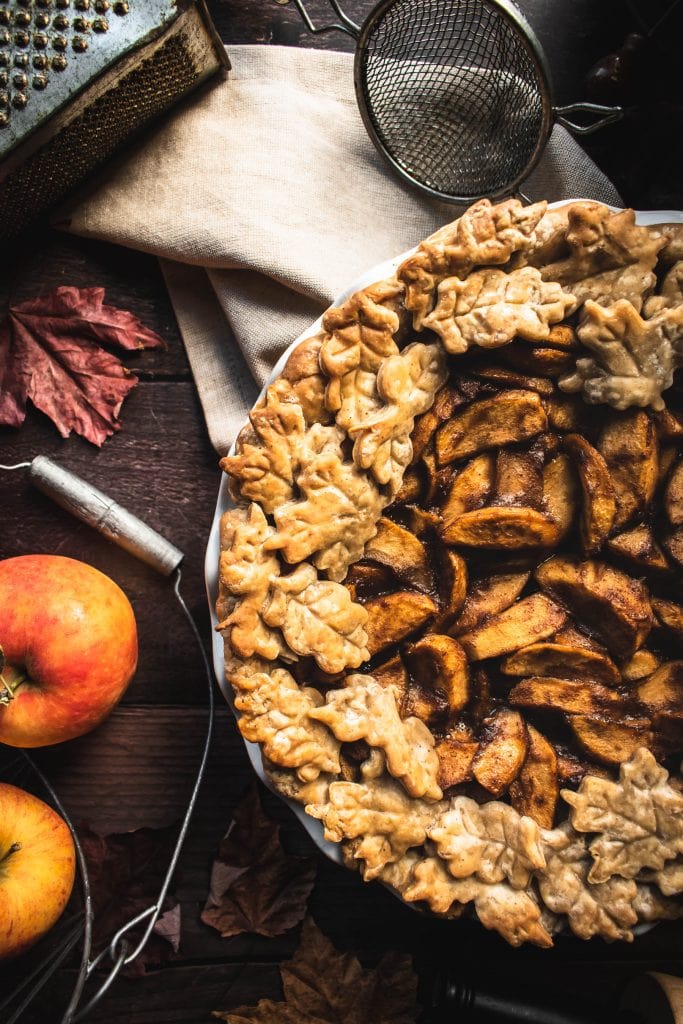 close up of the top of an Autumn fruit pie next to whole apples
