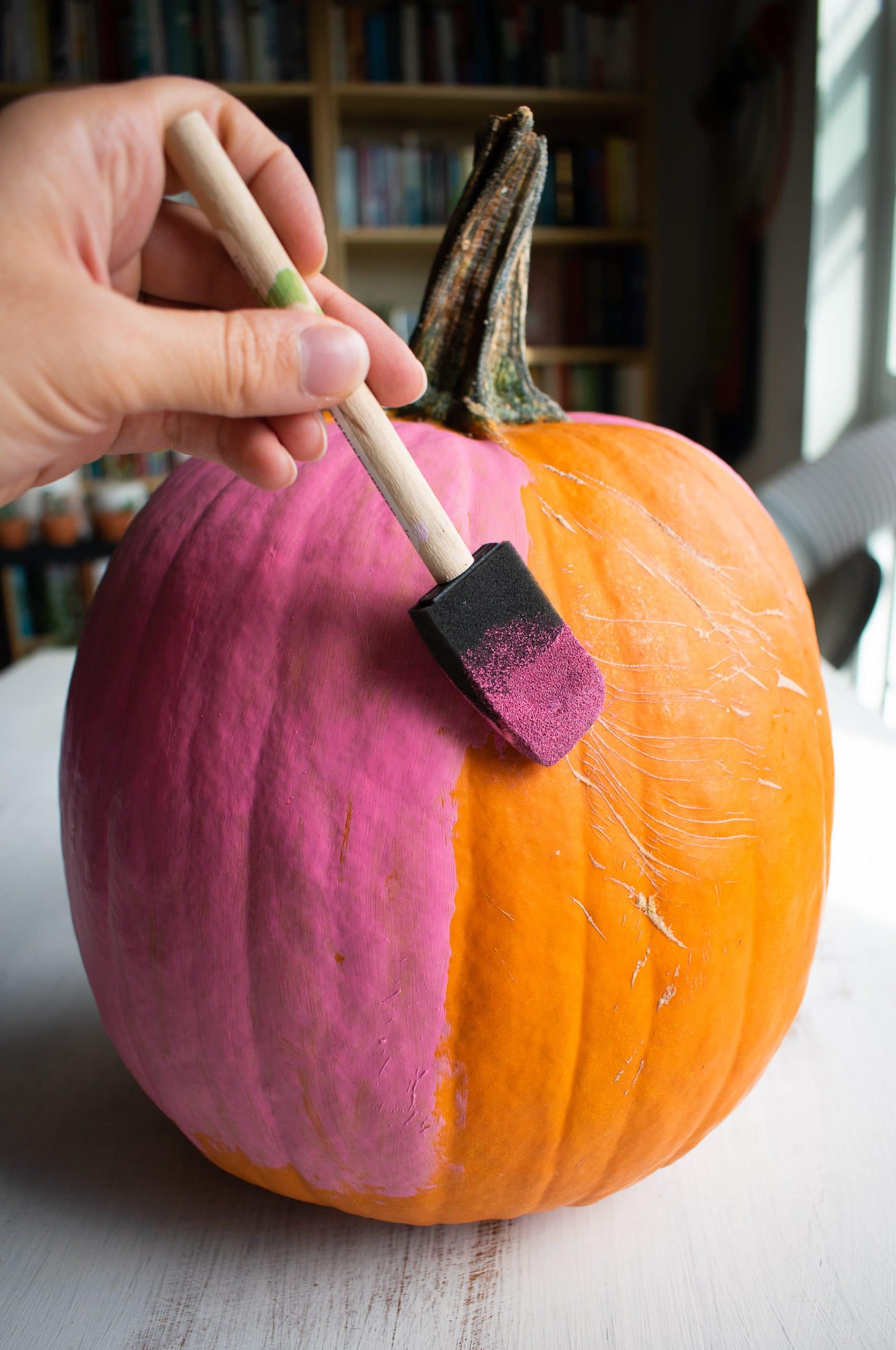 A hand painting pink paint onto a real pumpkin.