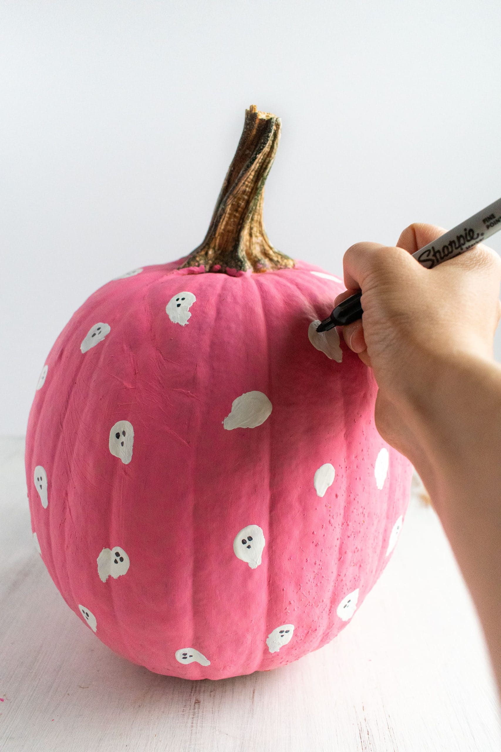 A hand drawing ghost faces on a cute DIY painted pumpkin.