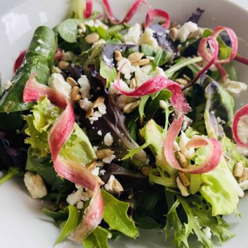 Pink ribbons of candied rhubarb on a salad in a white bowl.
