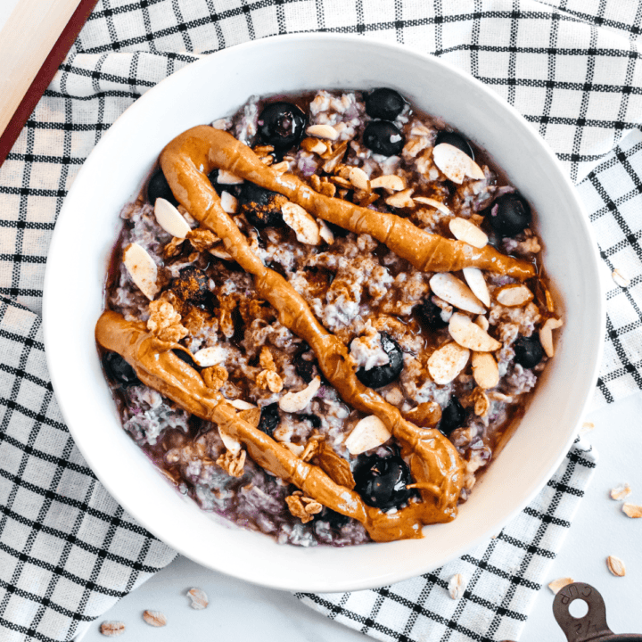 A white bowl filled with creamy oatmeal, blueberries, and chopped nuts, topped with a thick drizzle of nut butter.