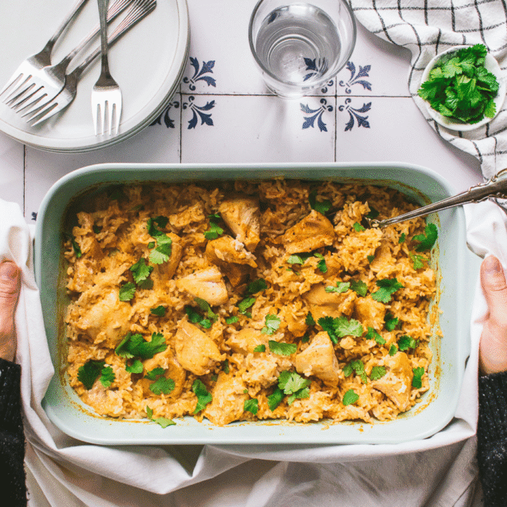 Two hands holding a baking dish filled with baked chicken and rice.
