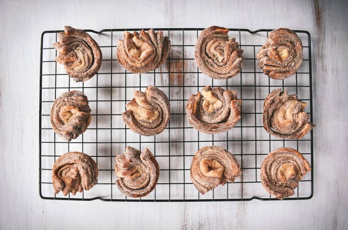 A dozen baked cruffins on a wire cooling rack.