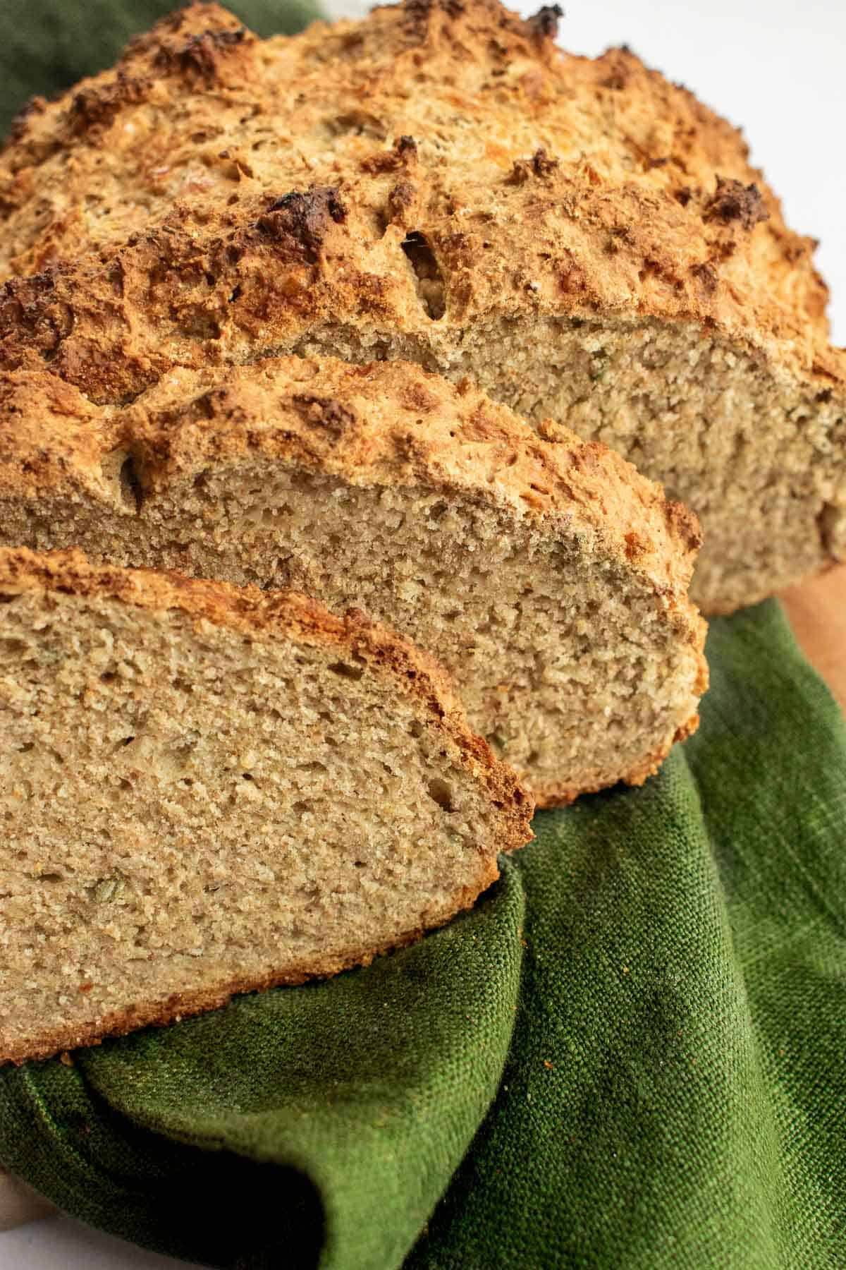 Two slices of crusty soda bread on a green linen next to the rest of the loaf.
