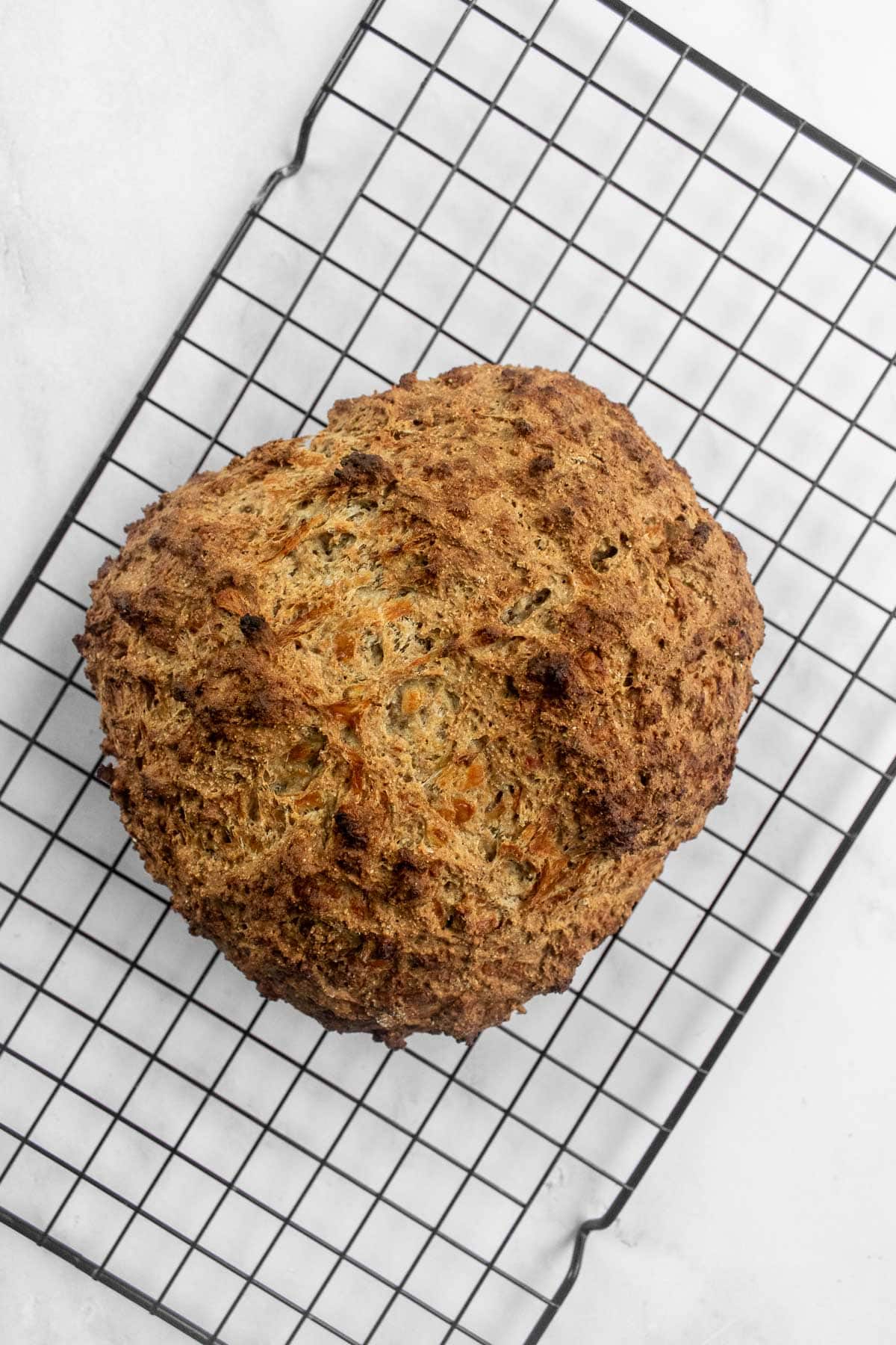 A loaf of baked soda bread on a wire cooling rack.