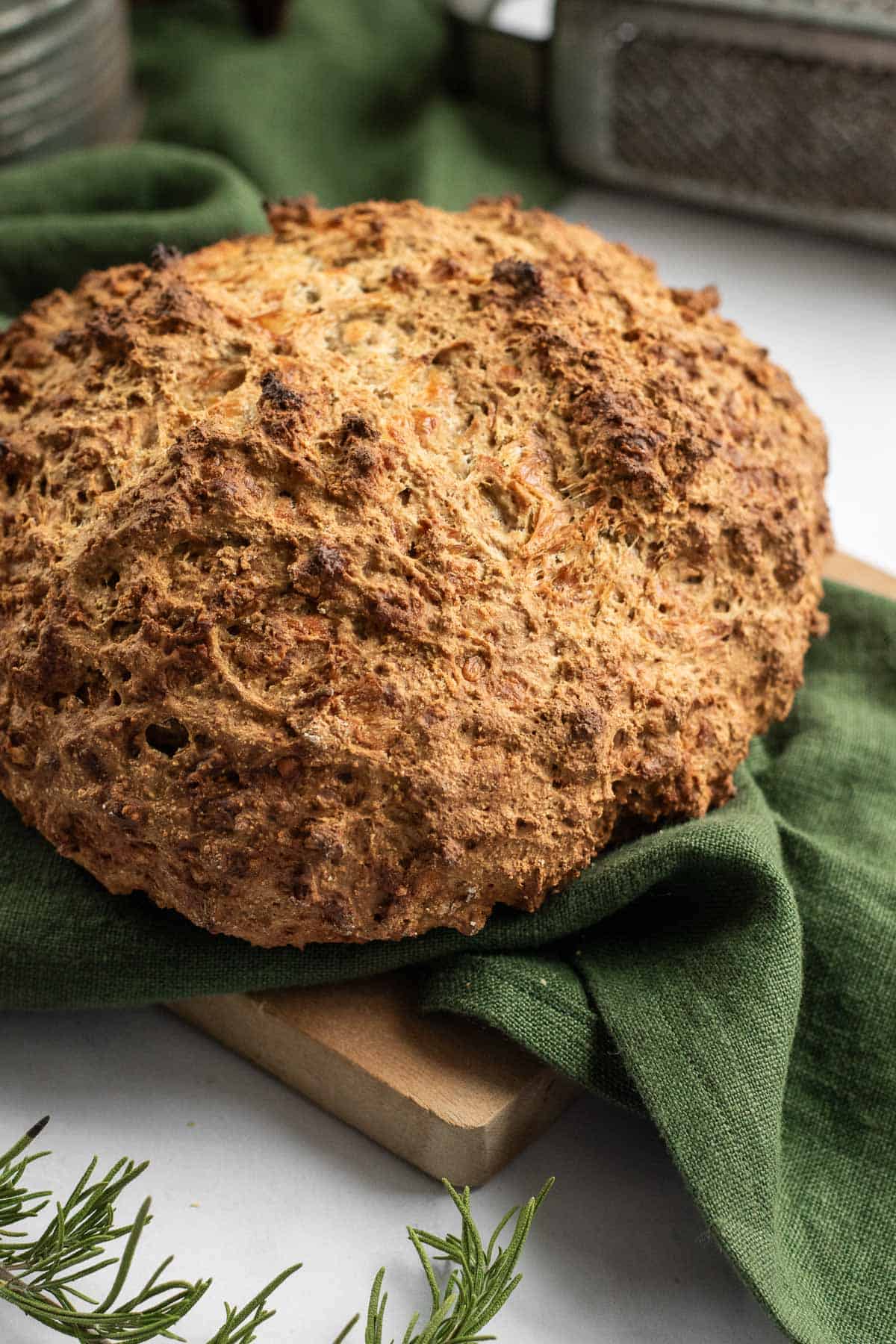 A whole loaf of crispy soda bread on a green linen on a wooden board.