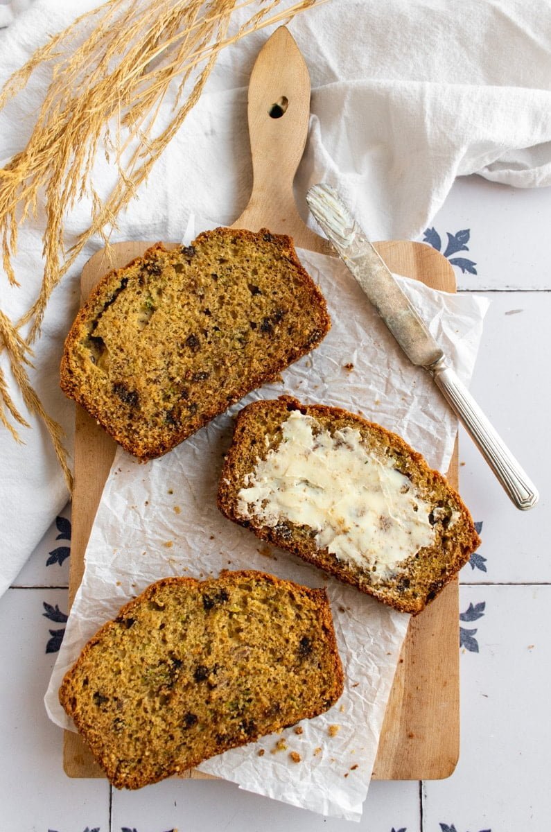 Three slices of banana zucchini chocolate chip bread on a cutting board, with one slice covered in butter.
