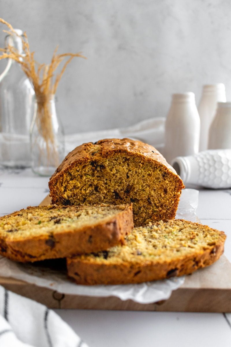 A sliced loaf of Banana Zucchini Chocolate Chip Bread on parchment paper on a wood board.