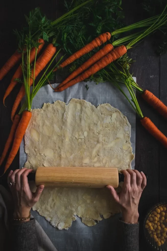Two hands rolling out pie crust on parchment paper.