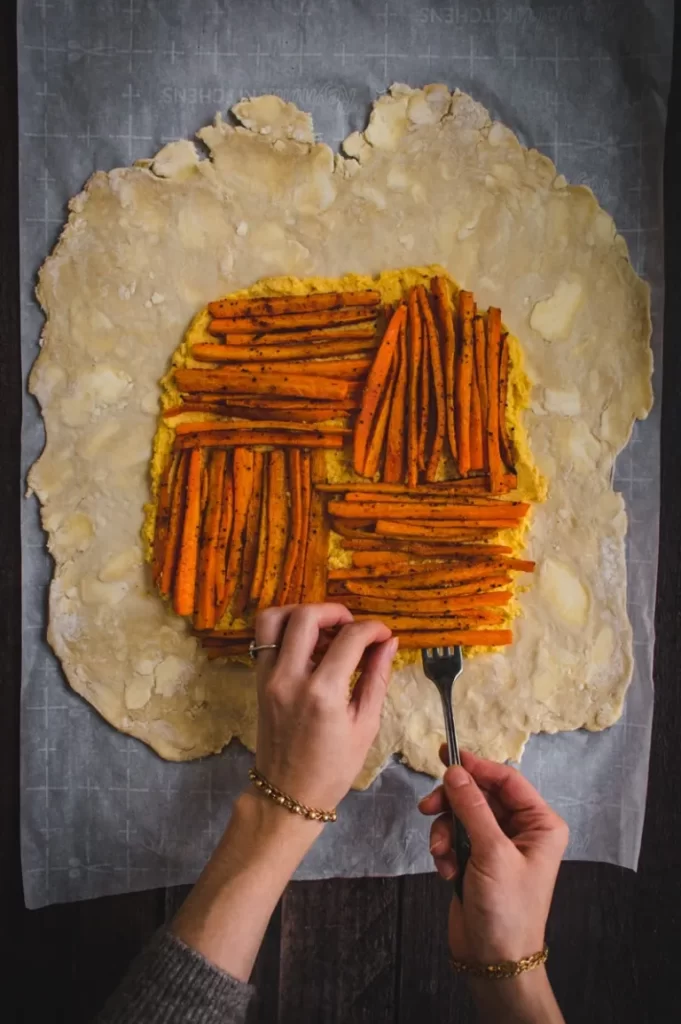Two hands arranging roasted carrots on pie dough.
