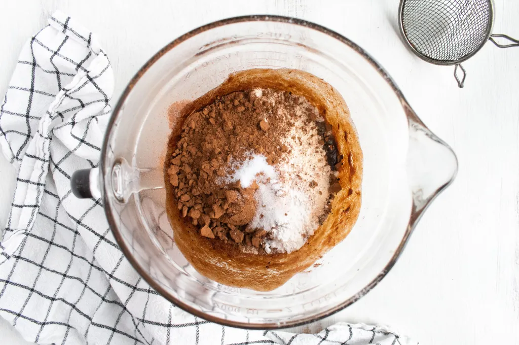 Cocoa powder, granulated sugar, and flour sprinkled in a glass mixing bowl.