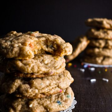A stack of four chunky rainbow sprinkle cookies on a dark table.