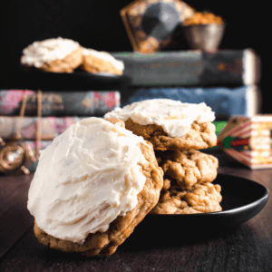 Four chunky butterbeer cookie stacked on a black plate topped with white frosting.