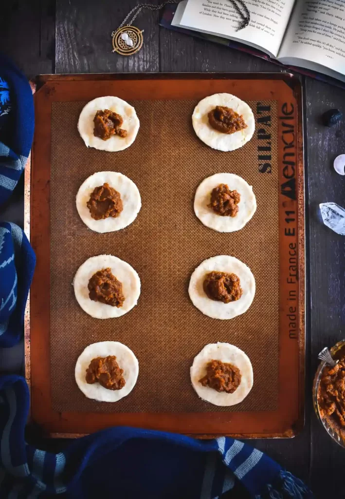 Circles of pie dough topped with pumpkin filling on a sheet pan.