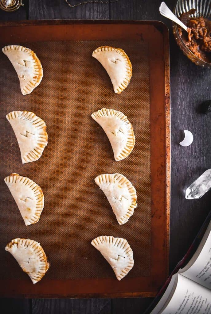 Eight unbaked half-circle pasties on a sheet pan.