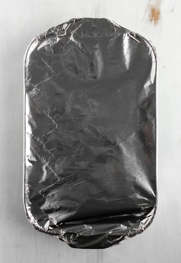 A baking dish covered in aluminum foil on a light surface.