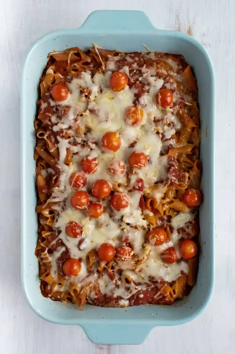 Baked pasta in a baking pan with cherry tomatoes, minced garlic, and melted cheese on top.