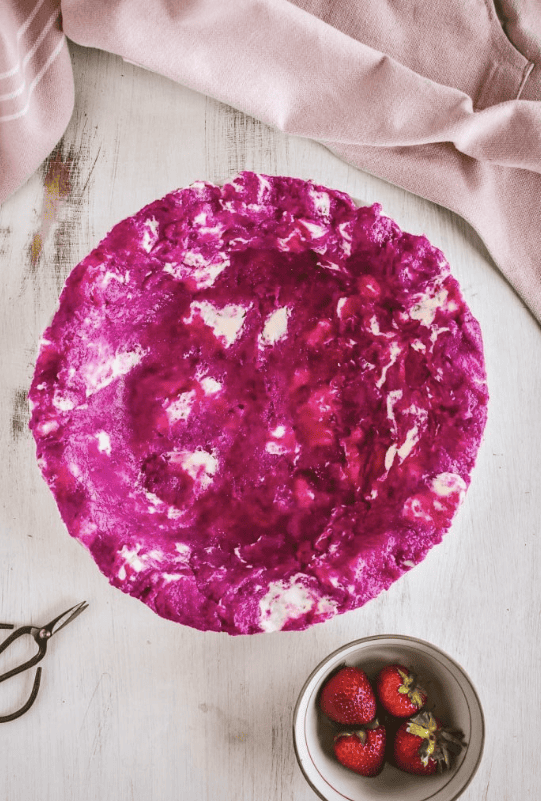 A pie dish filled with a bright pink buttery pie dough next to a bowl of strawberries.
