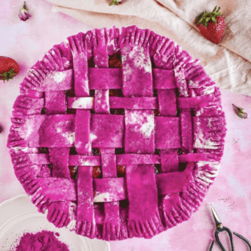 A dark pink unbaked pie on a pink table next to a plate of pitaya powder, strawberries, and a light pink linen.