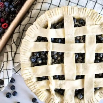 Blueberry pie on a table with a box of berries.