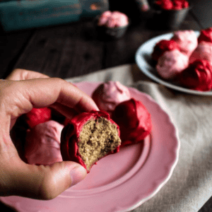 A hand holding a half-eaten bonbon coated in red chocolate.