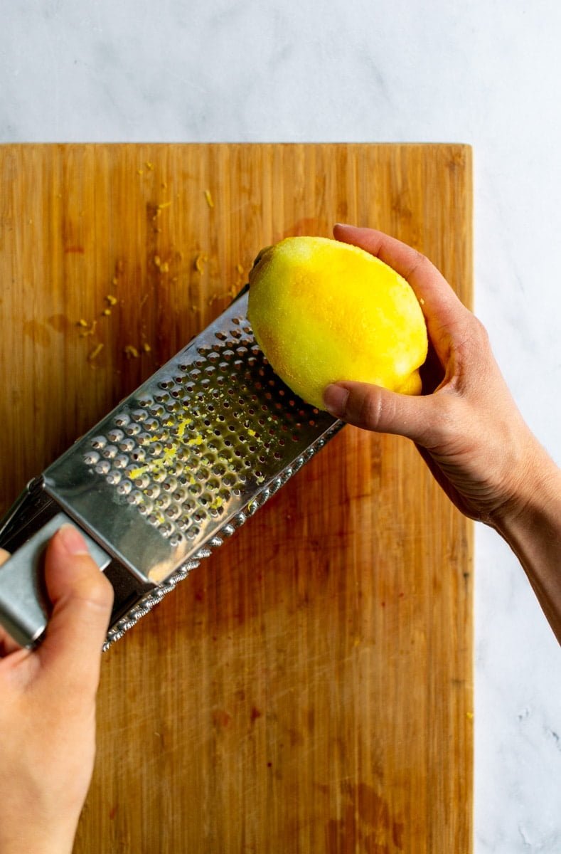 A hand zesting a lemon on a box grater.