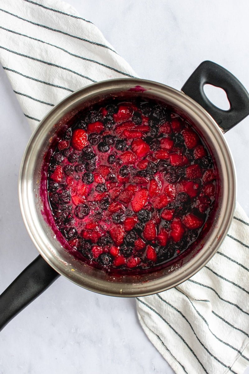 Simmered juicy berries in a metal saucepan on a black and white linen.