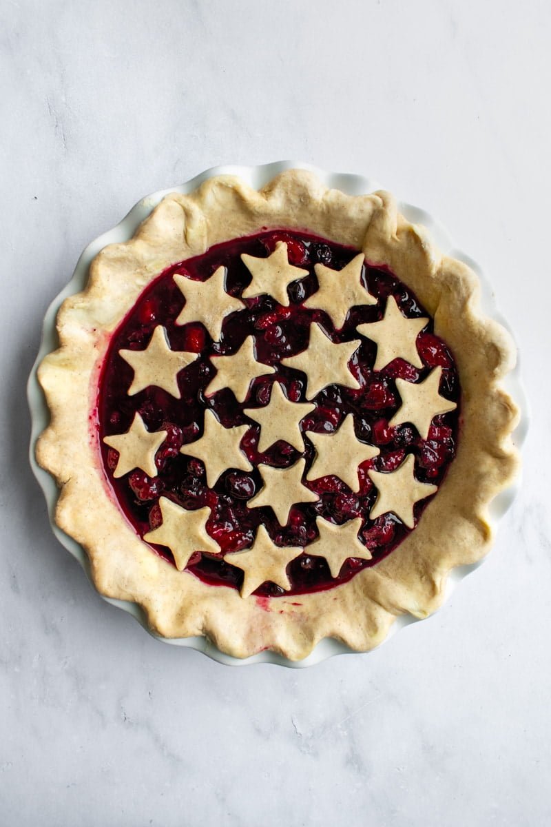 An unbaked pie crust filled with thick, dark red berry filling in a white pie dish.
