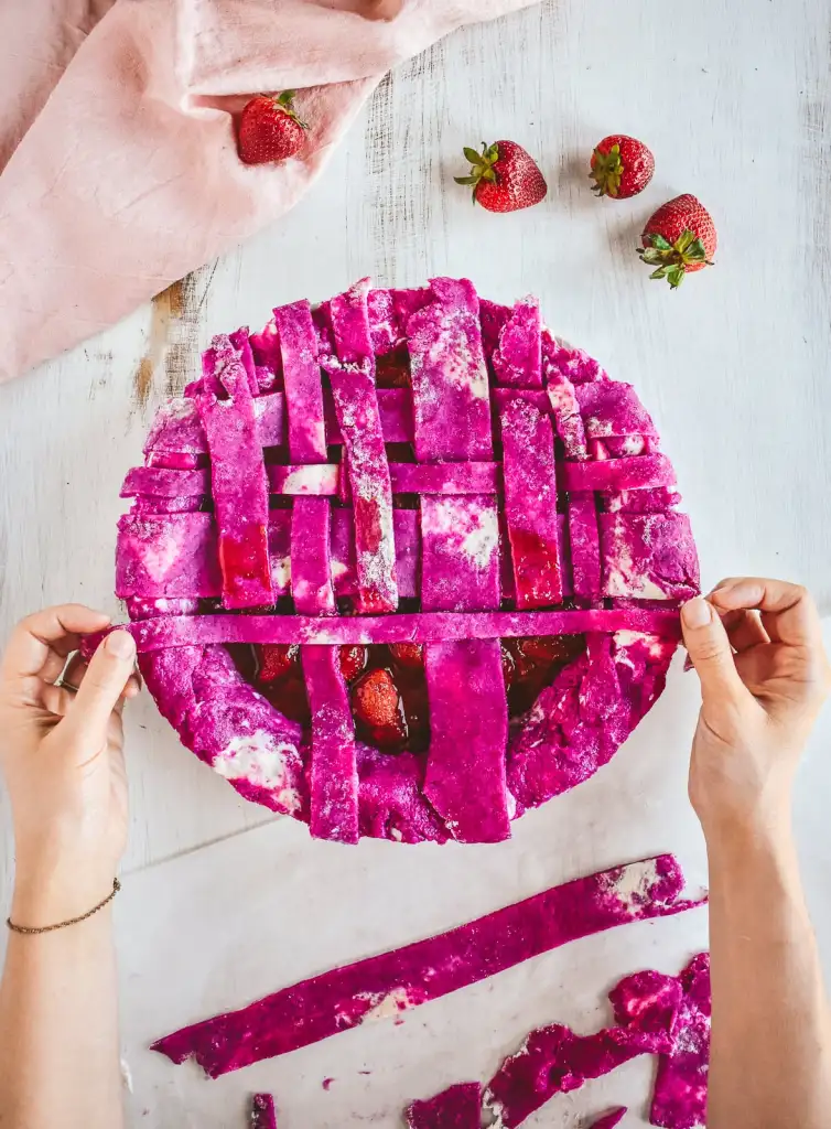 Lattice being adding to a raw strawberry pie on a light table.