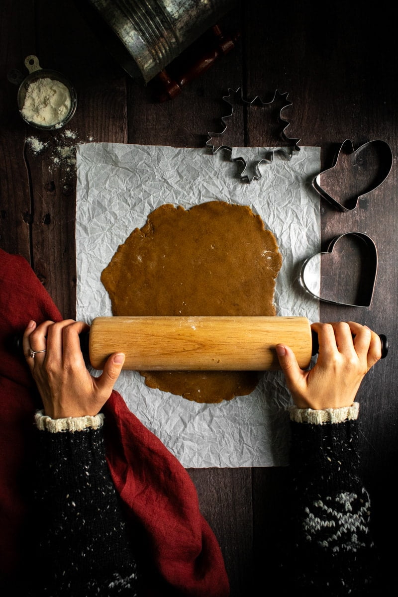 A girl in a Christmas sweater rolling out German Gingerbread Cookies dough. 