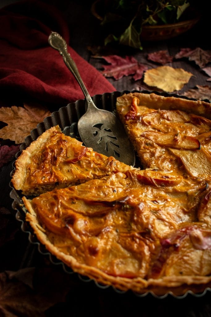 A sliced onion pie in a metal tart tin on a wooden table.