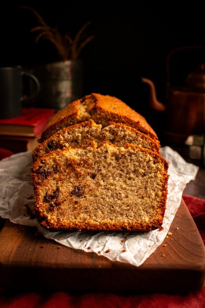 Slices of walnut loaf cake studded with chocolate chips on a wood board. 