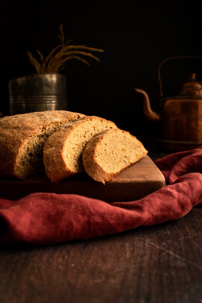 Slices of rye bread leaning against the rest of the loaf on a wood board on a red linen.