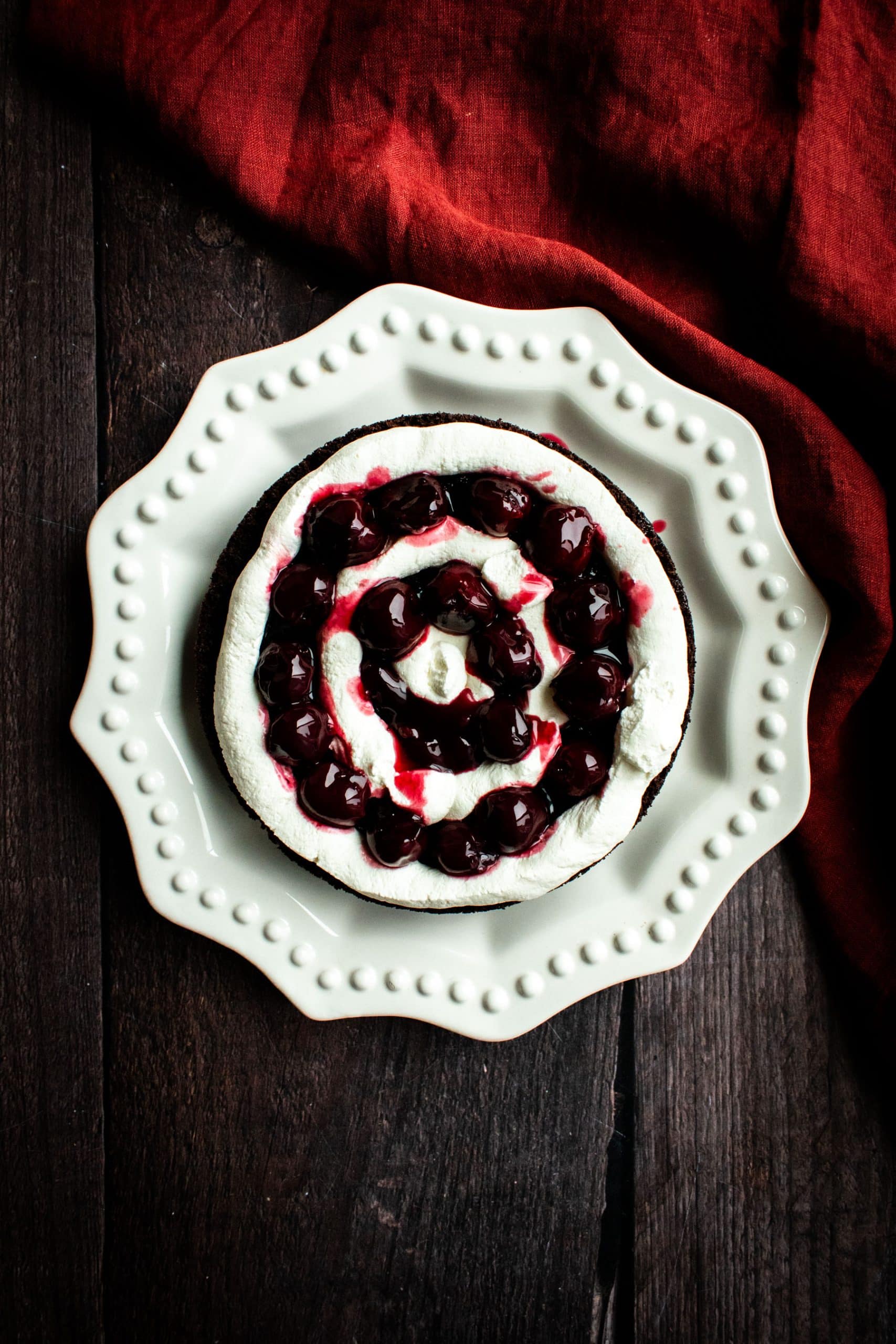 A chocolate cake topped with rings of whipped cream, canned cherries, and red cherry syrup.