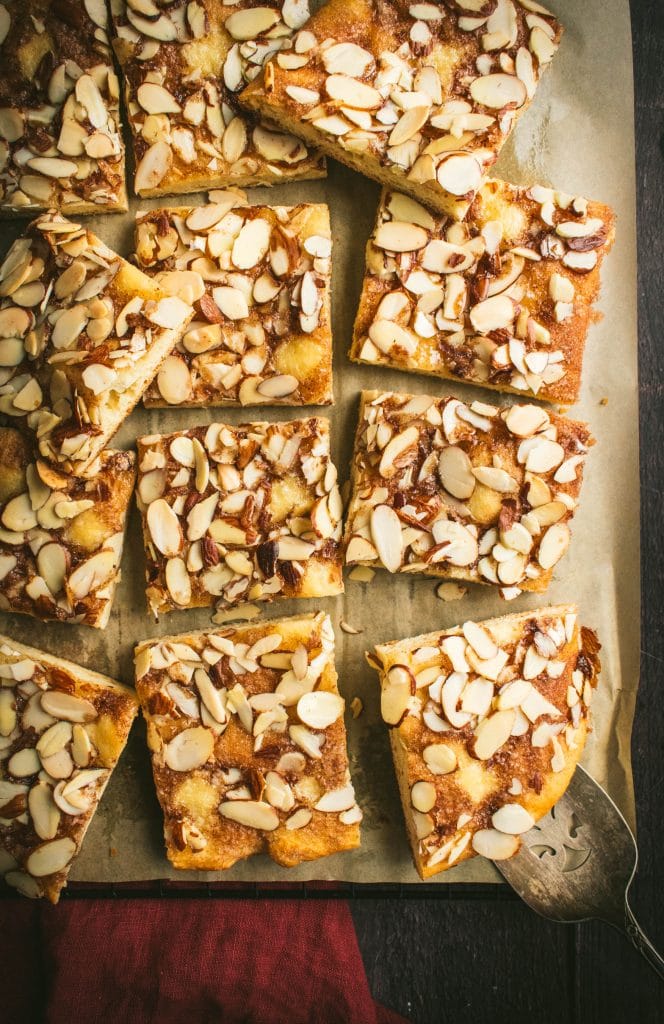 Squares of butter cake on parchment paper topped with sliced almonds.