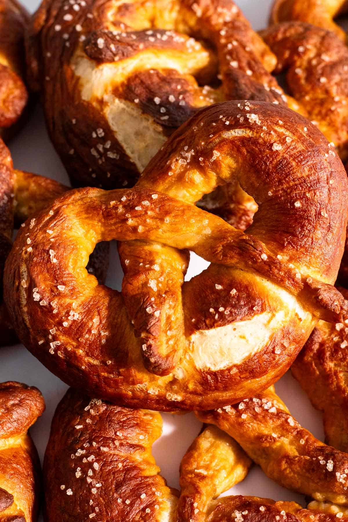 Half a dozen large soft pretzels piled on a light surface.