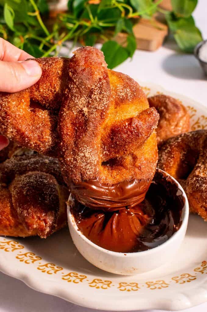 A hand dipping a cinnamon pretzel into a dish of melted chocolate.