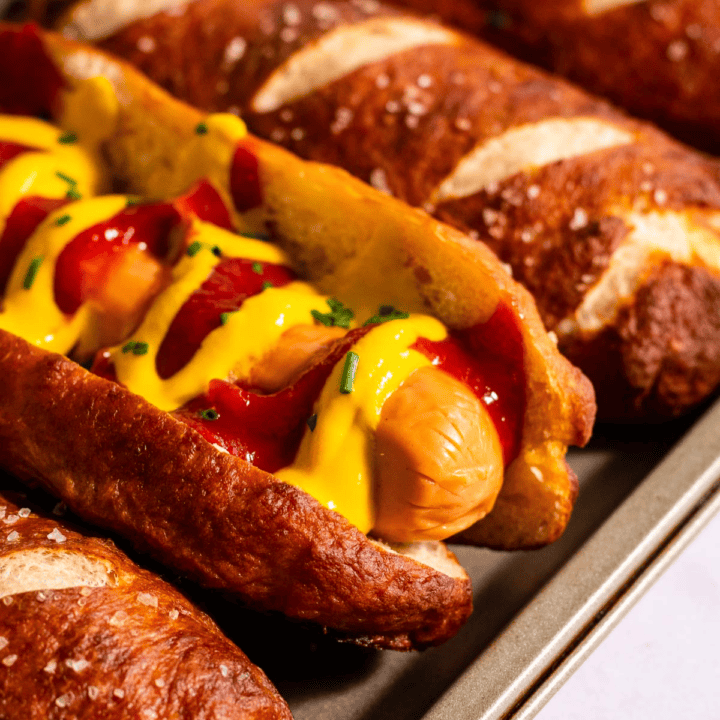 Hot dog buns arranged on a metal baking sheet, with one bun filled with a hot dog topped with ketchup and mustard.