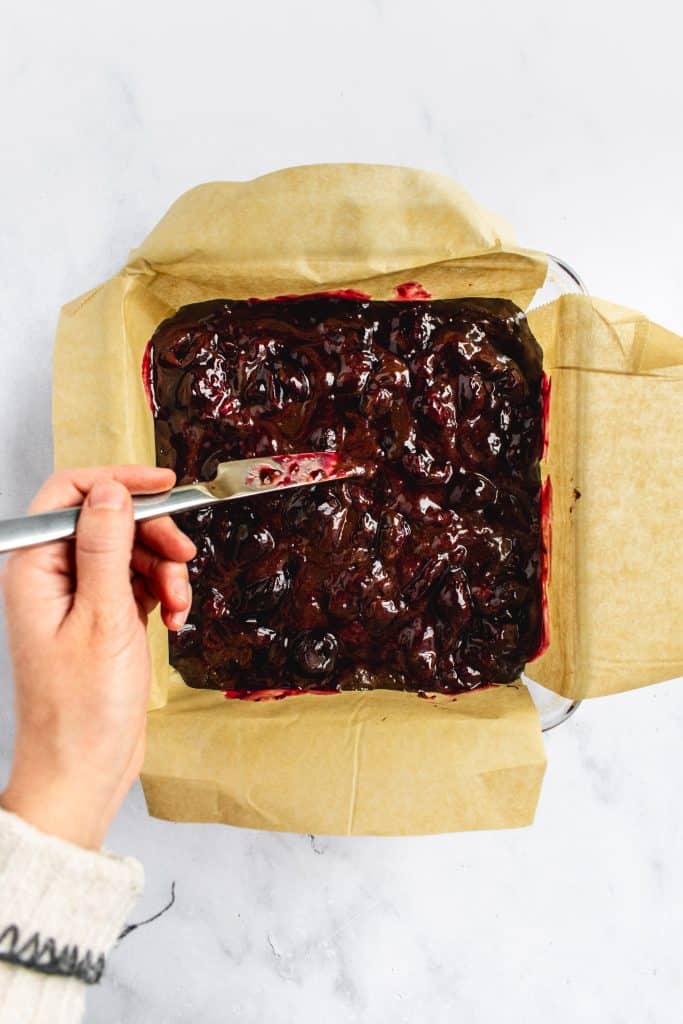 A hand swirling cherry sauce into brownie batter.