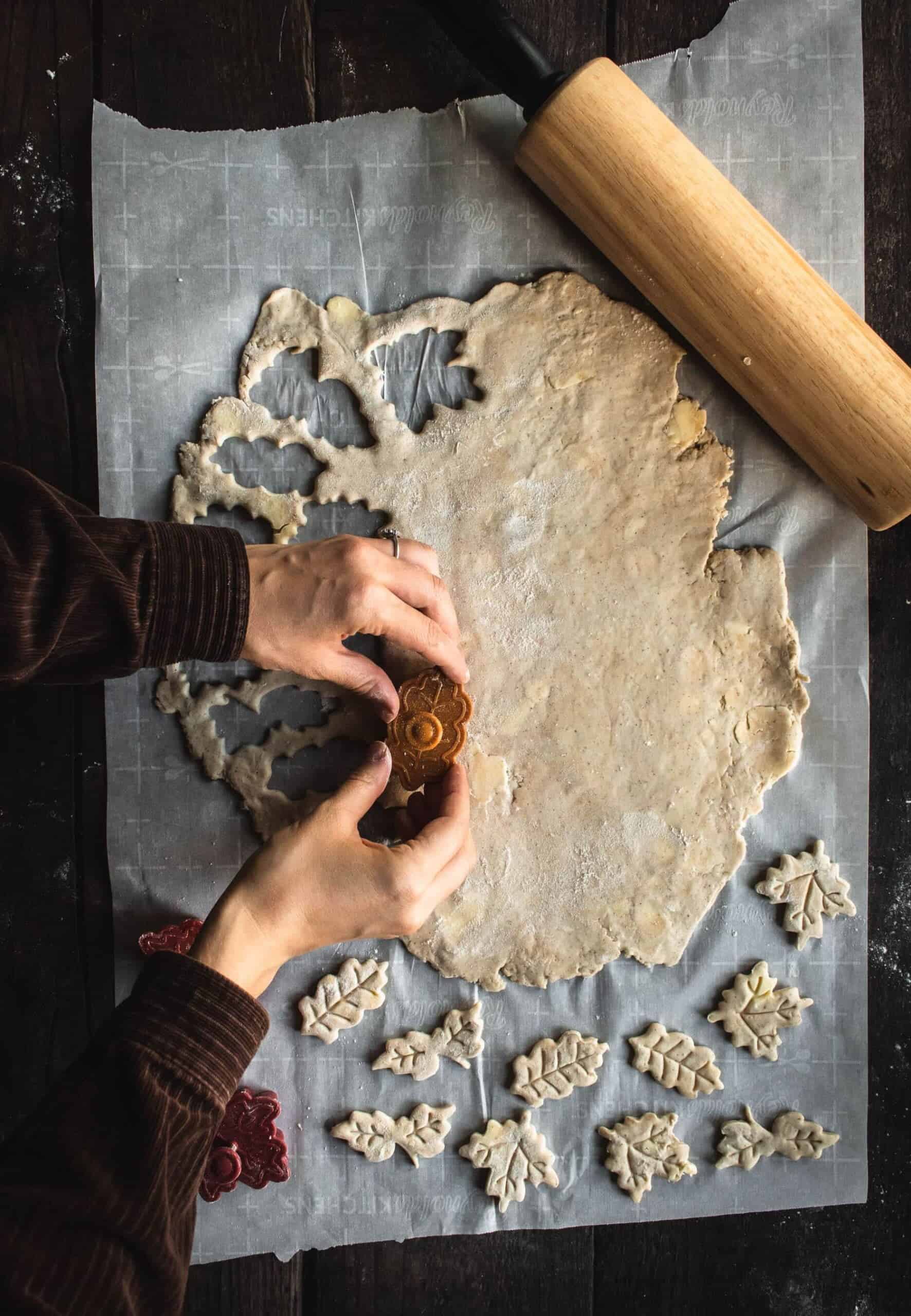 Two hands cutting out leaf cut-outs in pie dough.