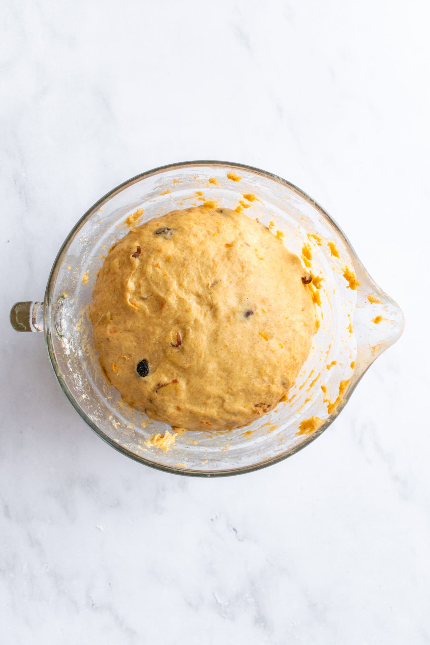 Risen bread dough in a glass mixing bowl with raisins and sliced almonds folded into it.