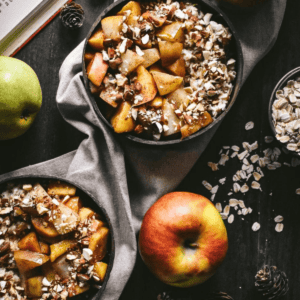 Two bowls of oatmeal topped with stewed apples, chopped nuts, and honey.