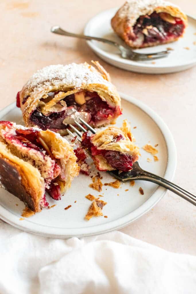 A half-eaten slice of cherry strudel topped with powdered sugar on a small grey plate.